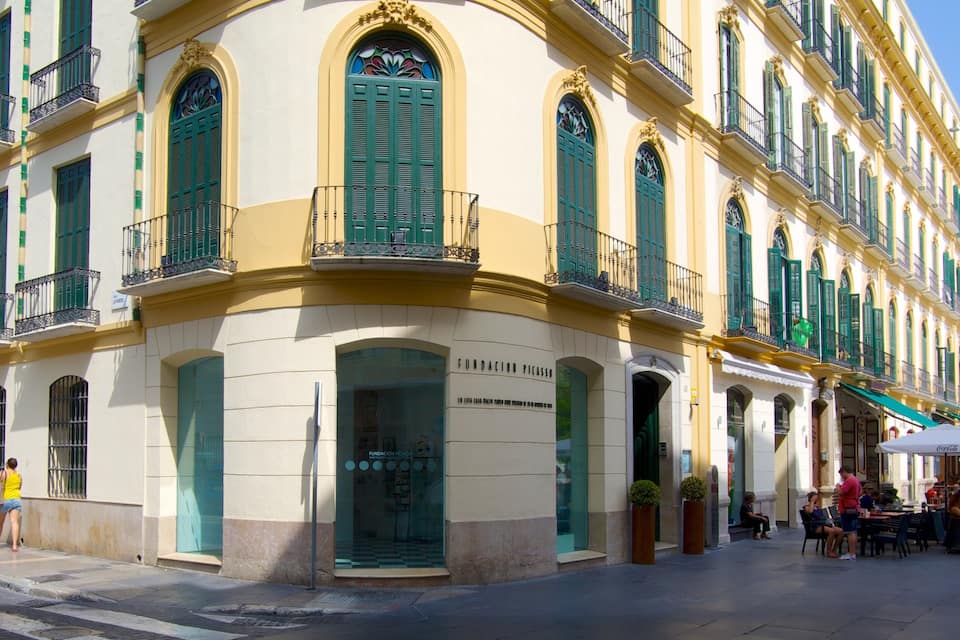 A historic building with green shutters and ornate balconies, a Coca-Cola sign, and outdoor seating.