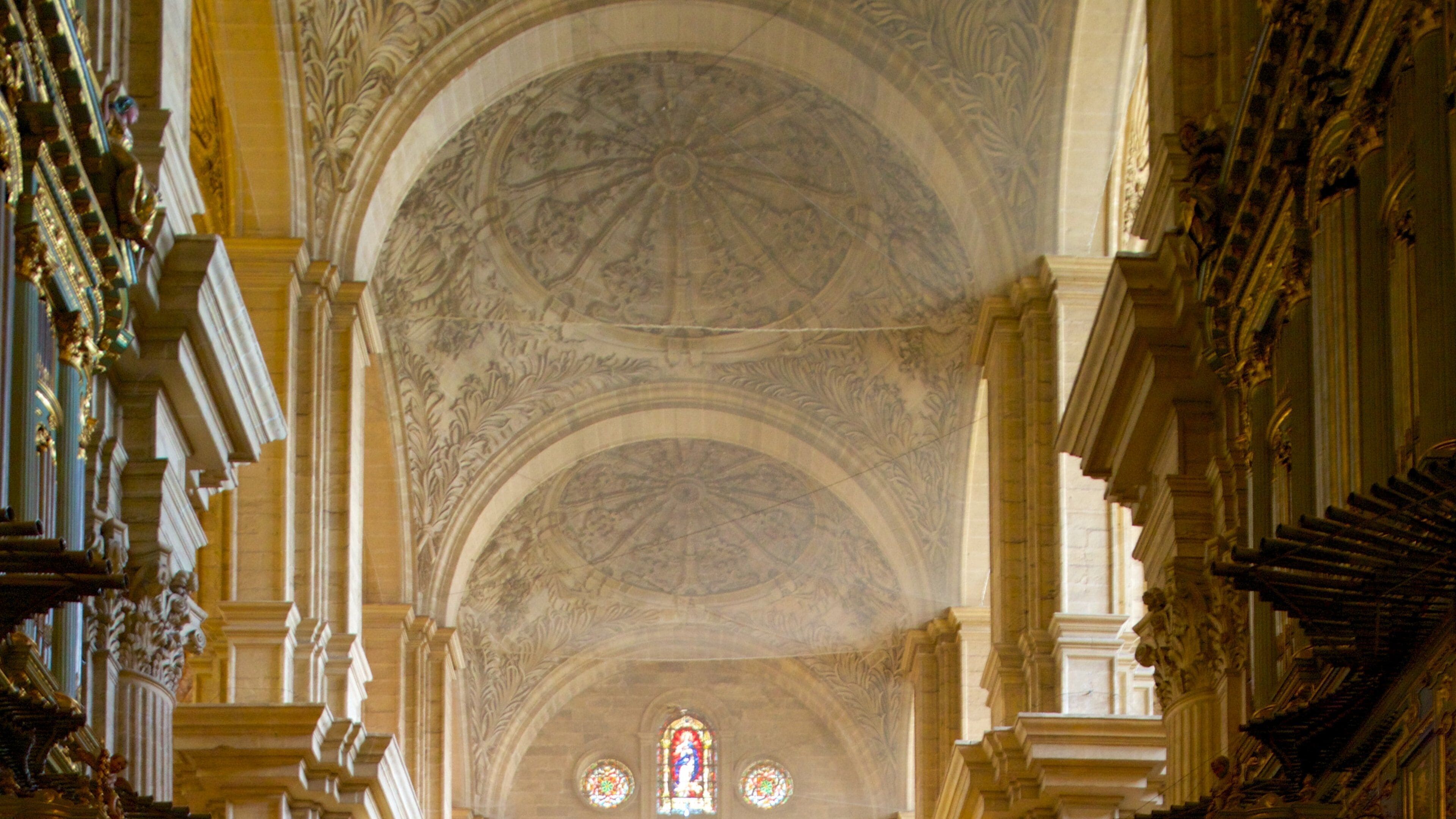 L’intérieur d’une église richement décorée, avec une voûte élevée, des motifs complexes peints au plafond et des vitraux.