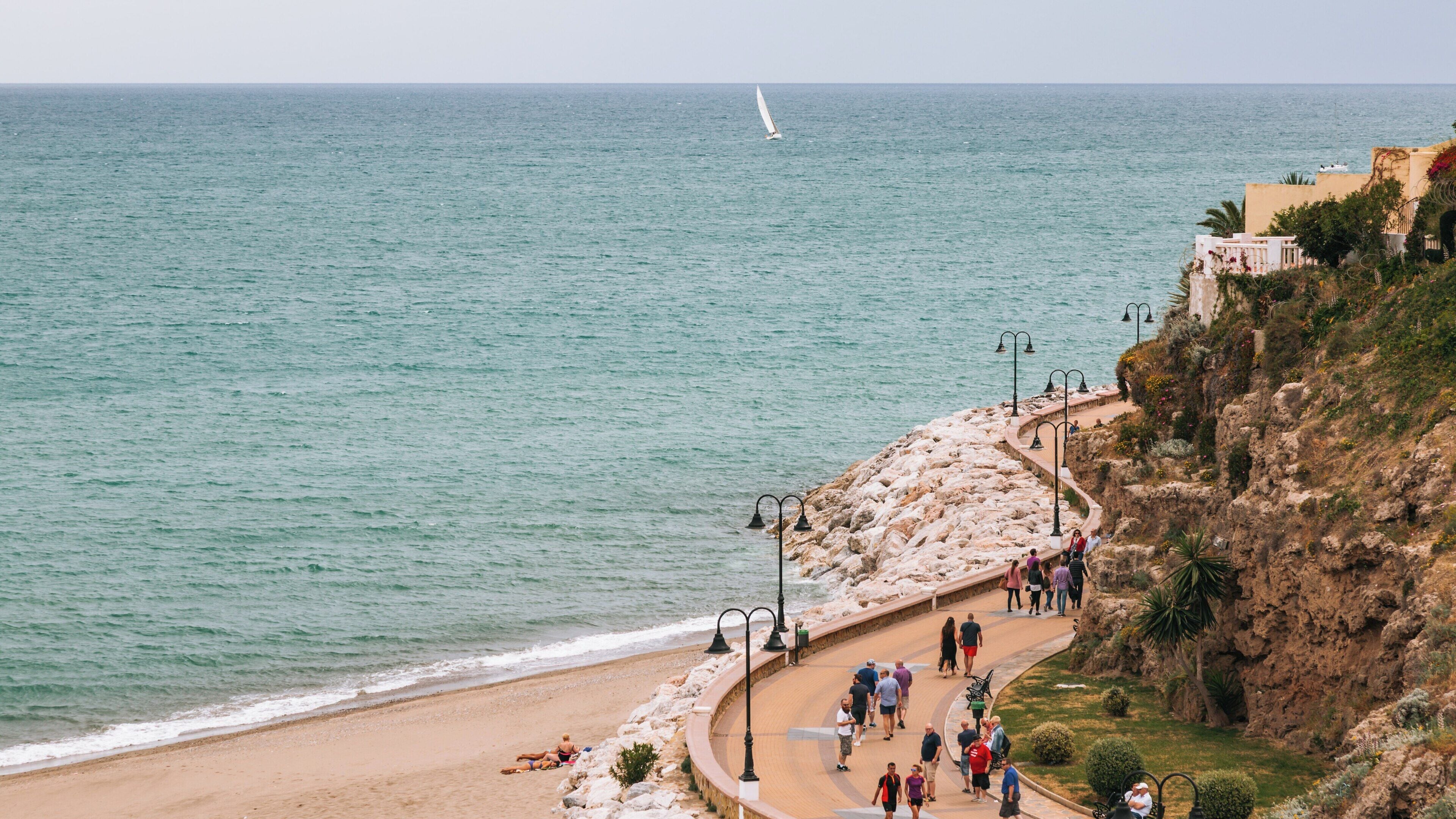 Relaxing stroll along Carihuela Beach in Torremolinos, Spain with beautiful views of the Mediterranean Sea and a distant sailboat