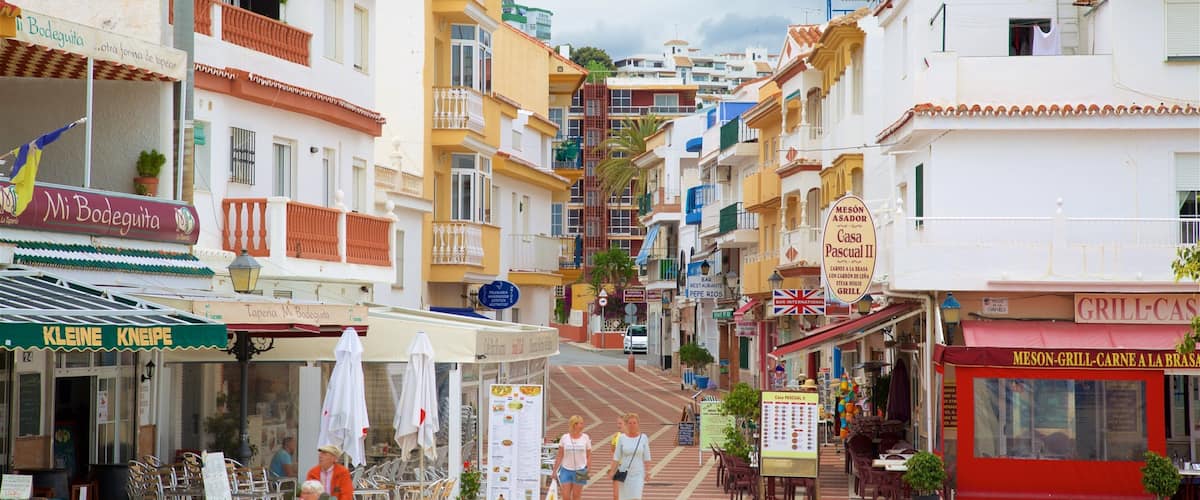 A narrow street lined with colorful buildings, outdoor seating, and various shops and restaurants.