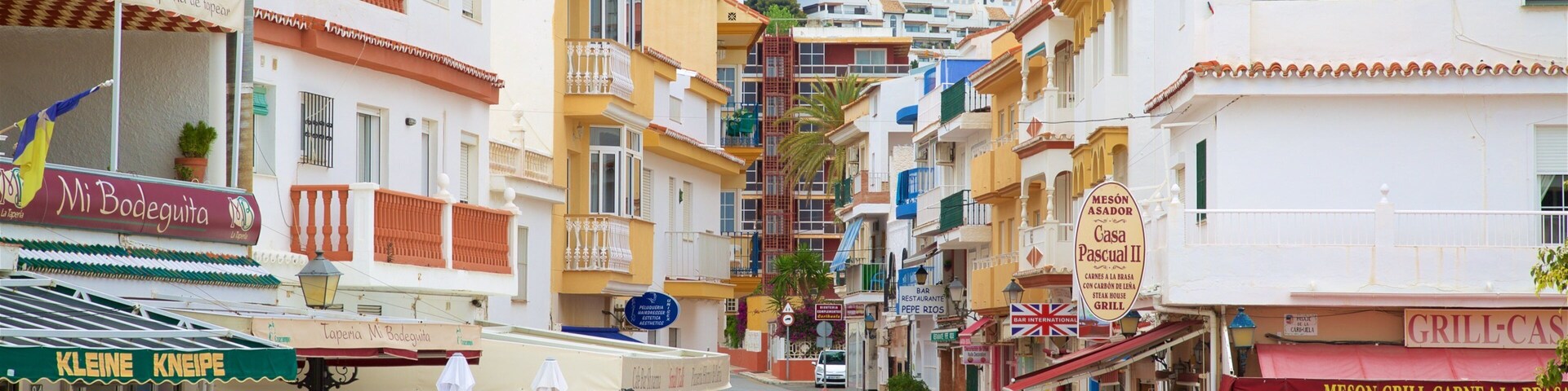 A narrow street lined with colorful buildings, outdoor seating, and various shops and restaurants.