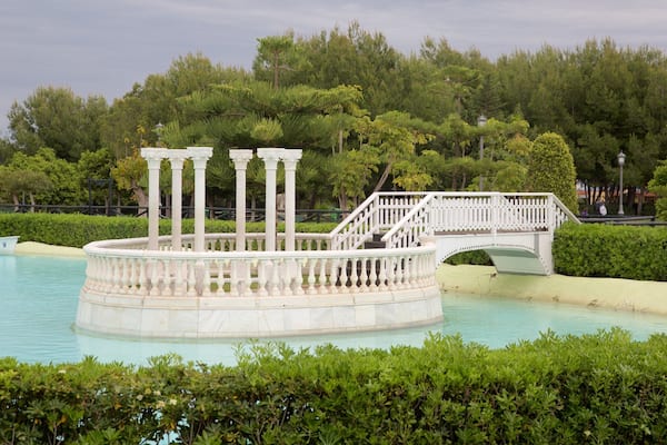 Ein kreisförmiger Brunnen mit Säulen, einer Brücke und üppigem Grün.