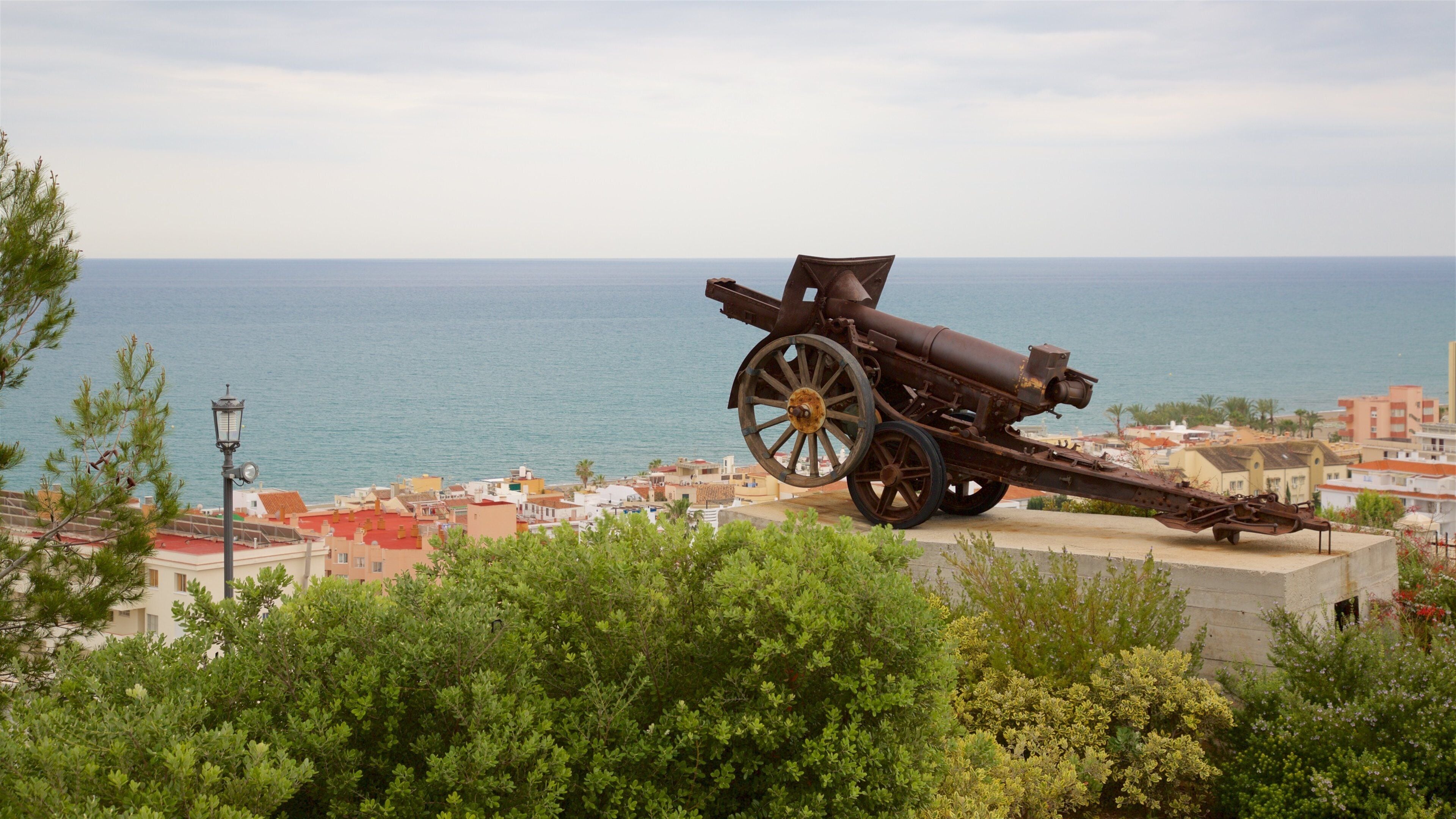 A large cannon overlooking a coastal town with buildings and the sea in the background.