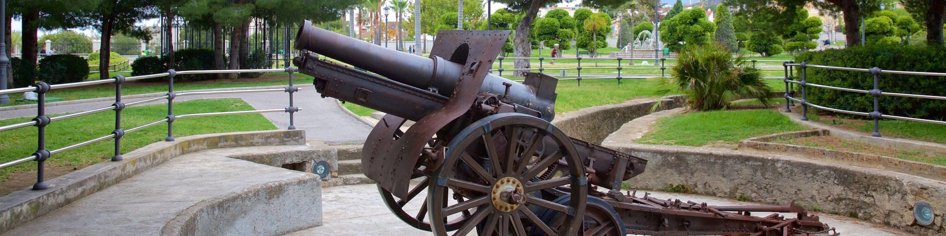 Un cañón grande en un parque con árboles y un camino pavimentado.