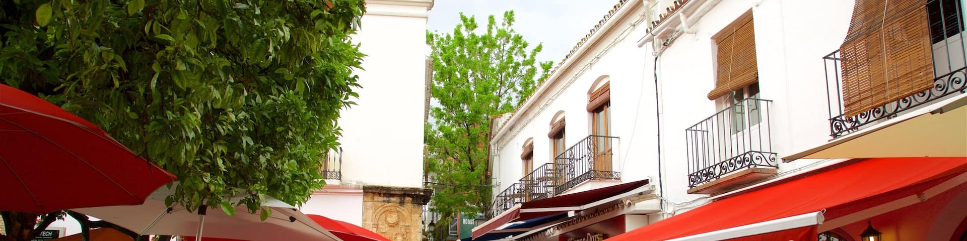 A narrow street with outdoor seating at cafes, red umbrellas, and traditional European architecture.