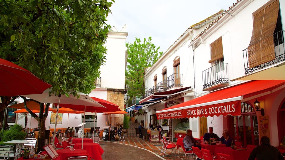 A narrow street with outdoor seating at cafes, red umbrellas, and traditional European architecture.