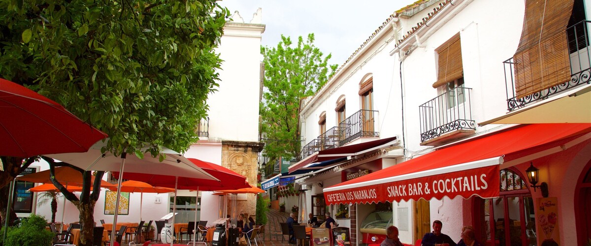 A narrow street with outdoor seating at cafes, red umbrellas, and traditional European architecture.