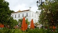 Un bâtiment blanc avec un toit recouvert de tuiles, entouré d’une végétation luxuriante et de parasols orange.