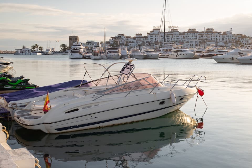 A marina with various boats docked, a cityscape in the background, and a clear sky.