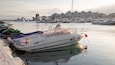 A marina with various boats docked, a cityscape in the background, and a clear sky.