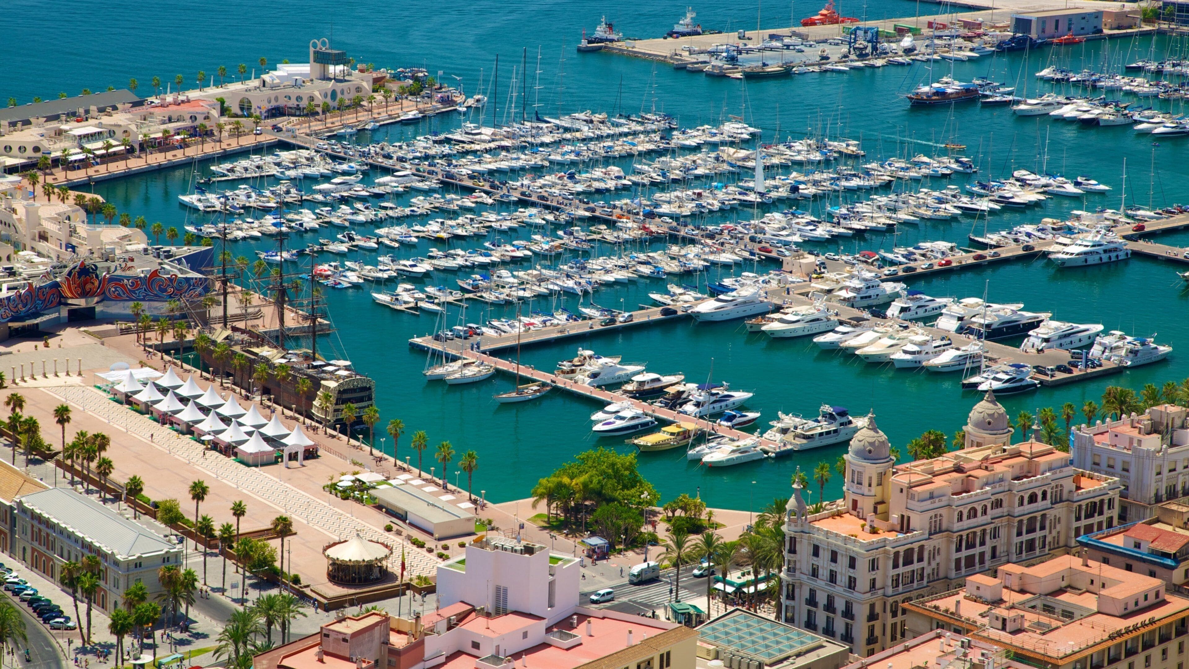 A marina filled with boats, a coastal promenade, and historic buildings.