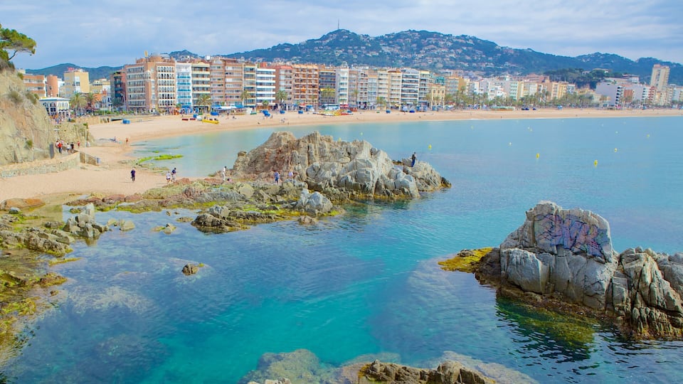 A coastal town with clear blue waters, rocky outcrops, and a sandy beach.