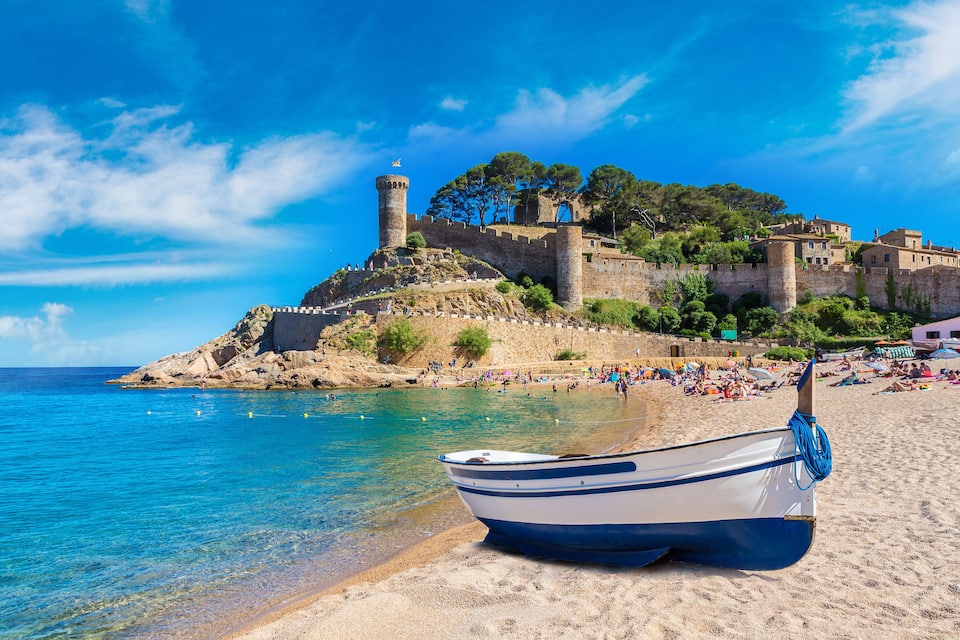 Un bateau sur une plage de sable, un château sur une colline et une mer bleue et limpide.