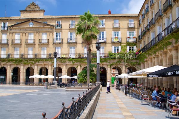 A historic building with arched windows and a clock, surrounded by outdoor seating and palm trees.