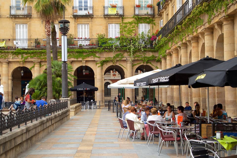 A bustling outdoor café with tables and chairs, surrounded by historic buildings with arches and balconies.