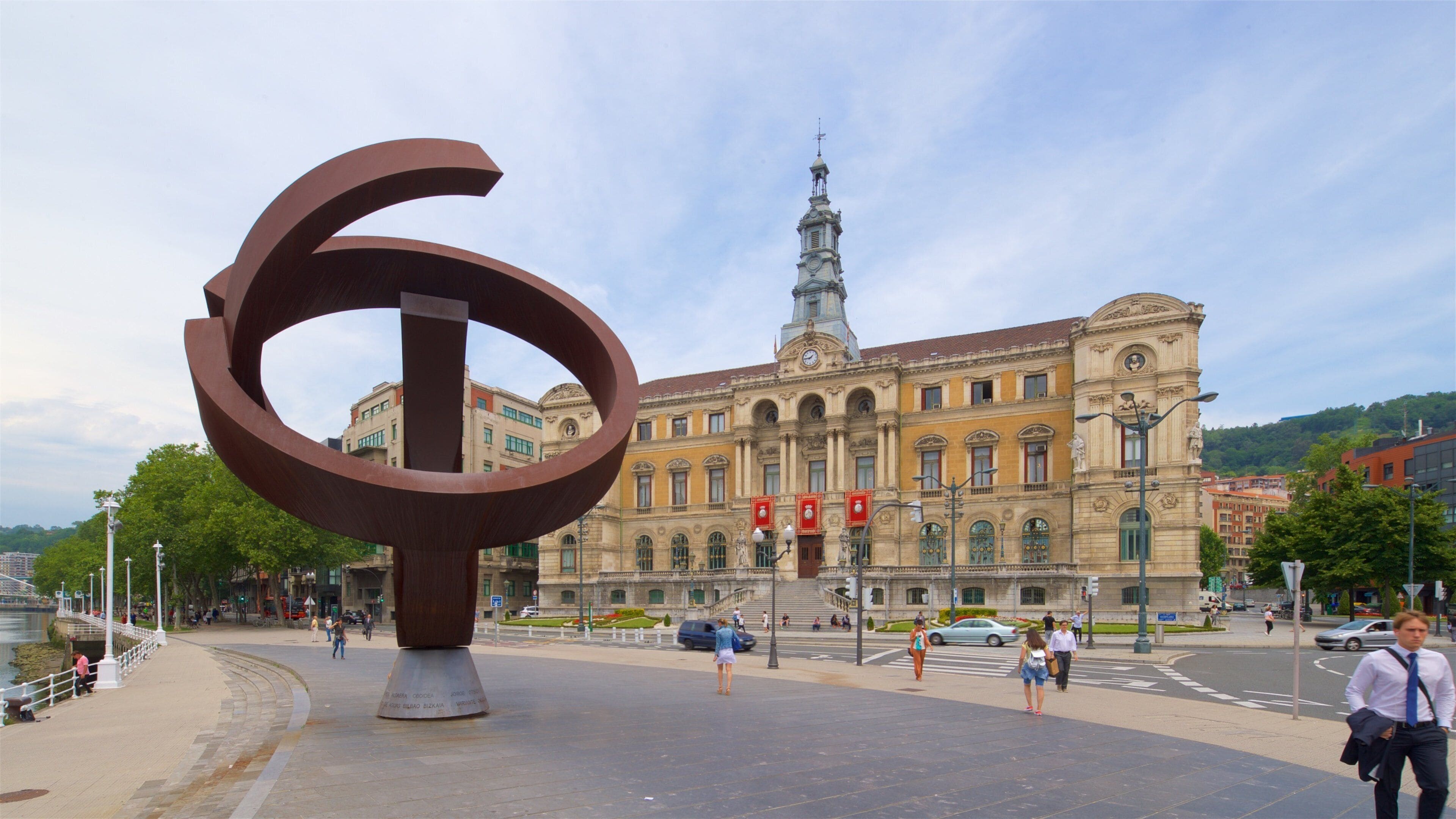 A large abstract sculpture in front of a historic building with a clock tower.