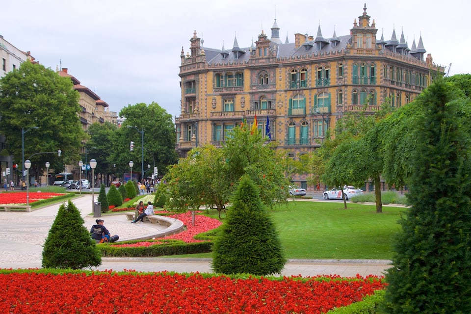 Un bâtiment historique à l’architecture riche et élaborée, entouré de jardins bien entretenus et agrémenté de fleurs rouges.
