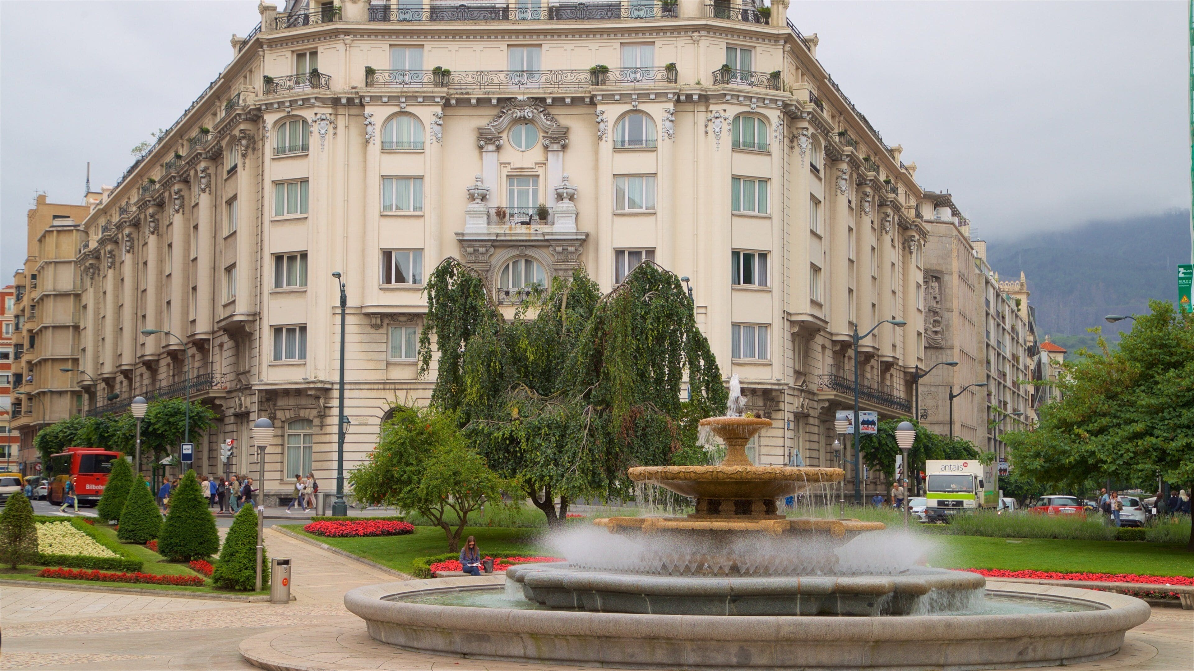 A historic building with ornate architecture, a central fountain, and surrounding greenery.