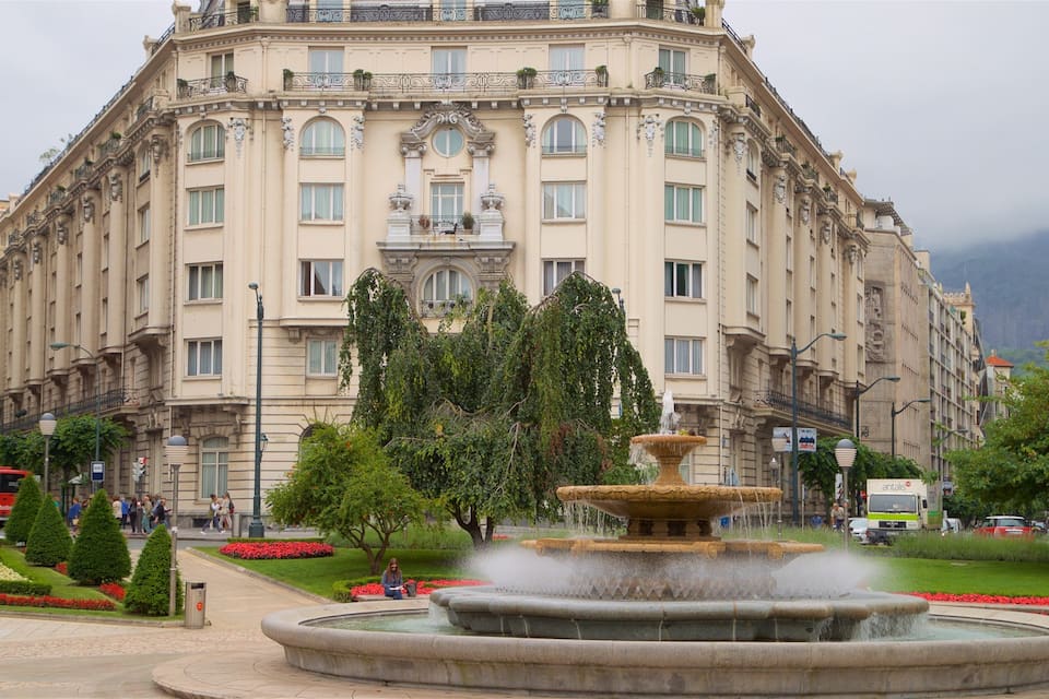 A historic building with ornate architecture, a central fountain, and surrounding greenery.