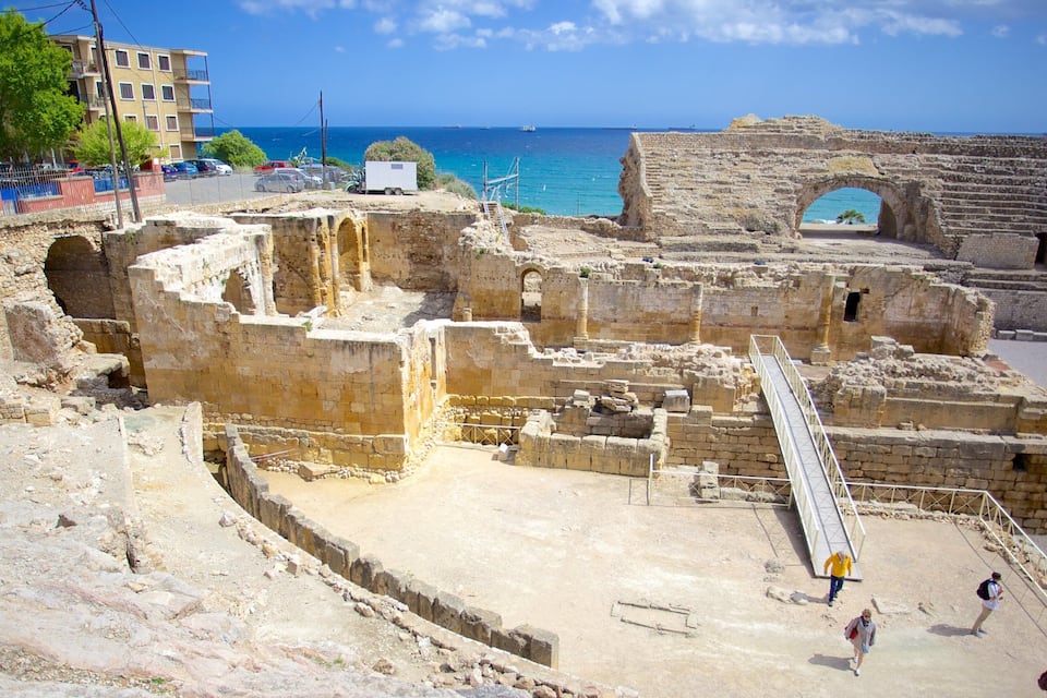 Rovine antiche con vista sul mare, tra cui un teatro e un ponte in pietra.