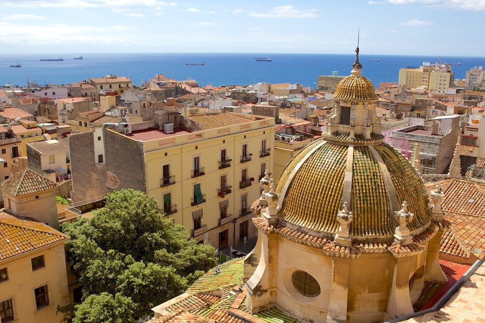 Paesaggio costiero con un edificio a cupola dorata ben visibile e navi all'orizzonte.