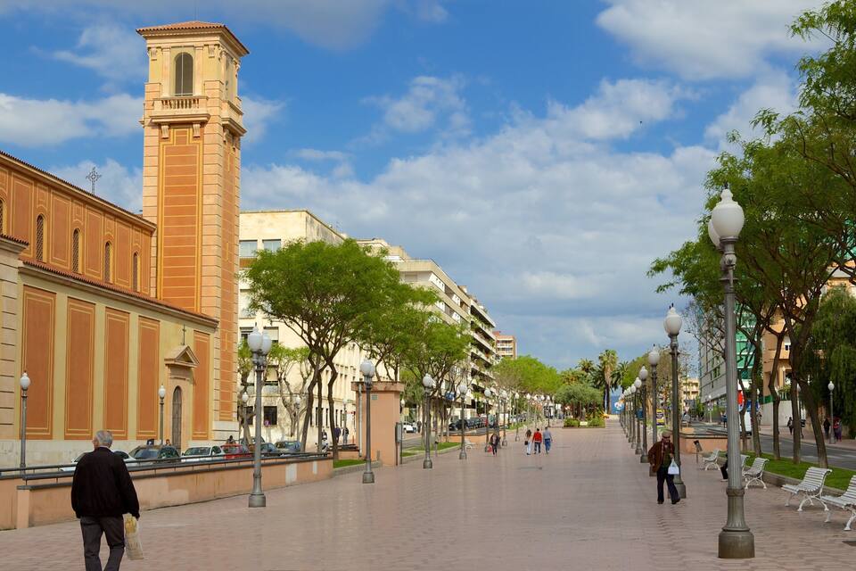 A wide pedestrian street lined with trees, benches, and street lamps.