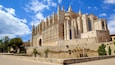 A historic cathedral with intricate Gothic architecture, a prominent bell tower, and a surrounding fortified wall.