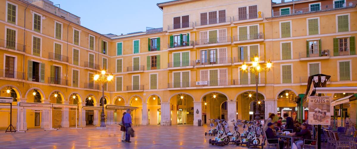 A spacious square with a yellow building, arched doorways, and a row of scooters.