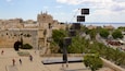 A historic cityscape with a prominent cathedral, a modern art installation, and a coastal view.