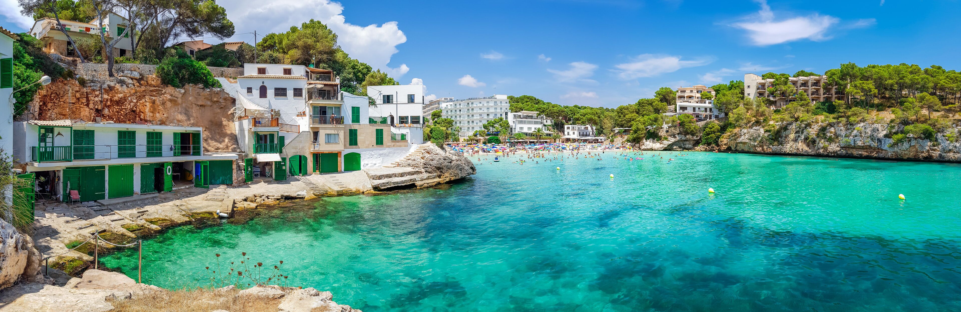 A coastal town with clear turquoise waters, a rocky shoreline, and buildings with green shutters.