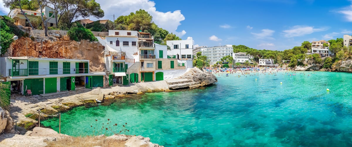 A coastal town with clear turquoise waters, a rocky shoreline, and buildings with green shutters.