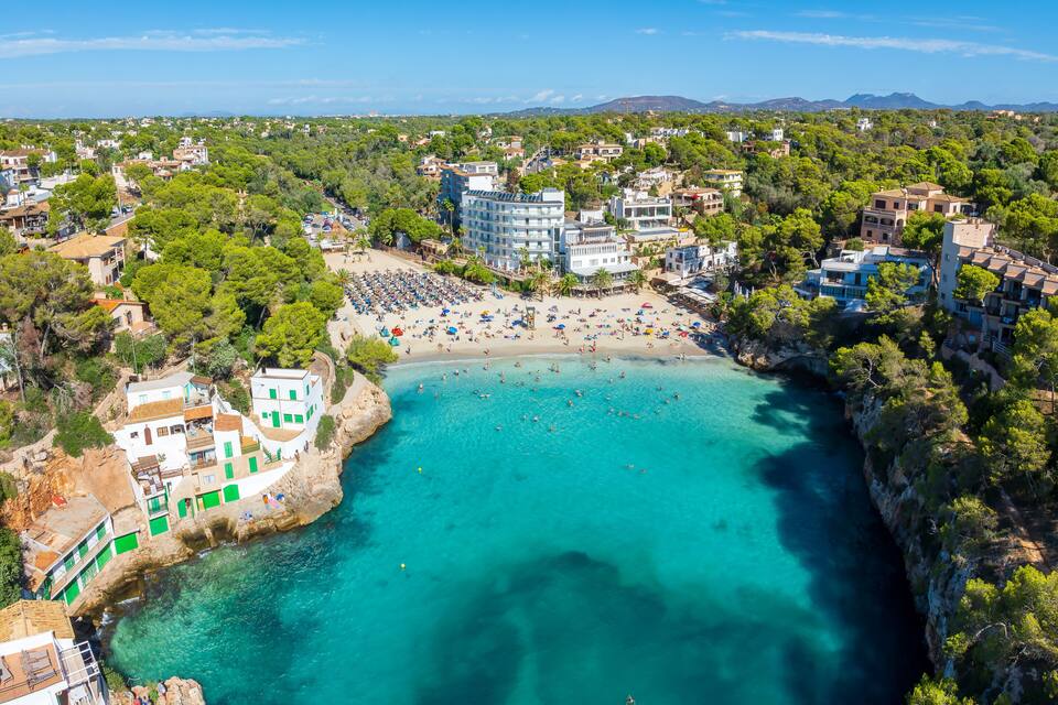 A coastal town with a beach, clear turquoise waters, and surrounding greenery.