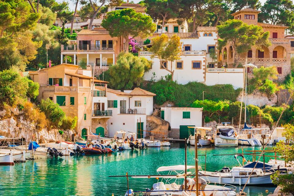 A coastal village with boats docked at a marina, surrounded by terraced buildings and lush greenery.