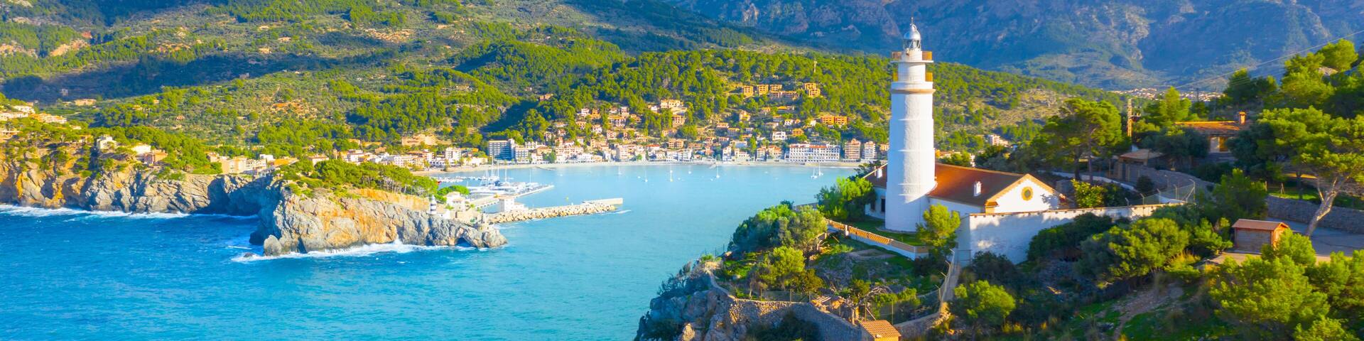 A coastal town with a prominent white lighthouse, rocky cliffs, and a clear blue sea.