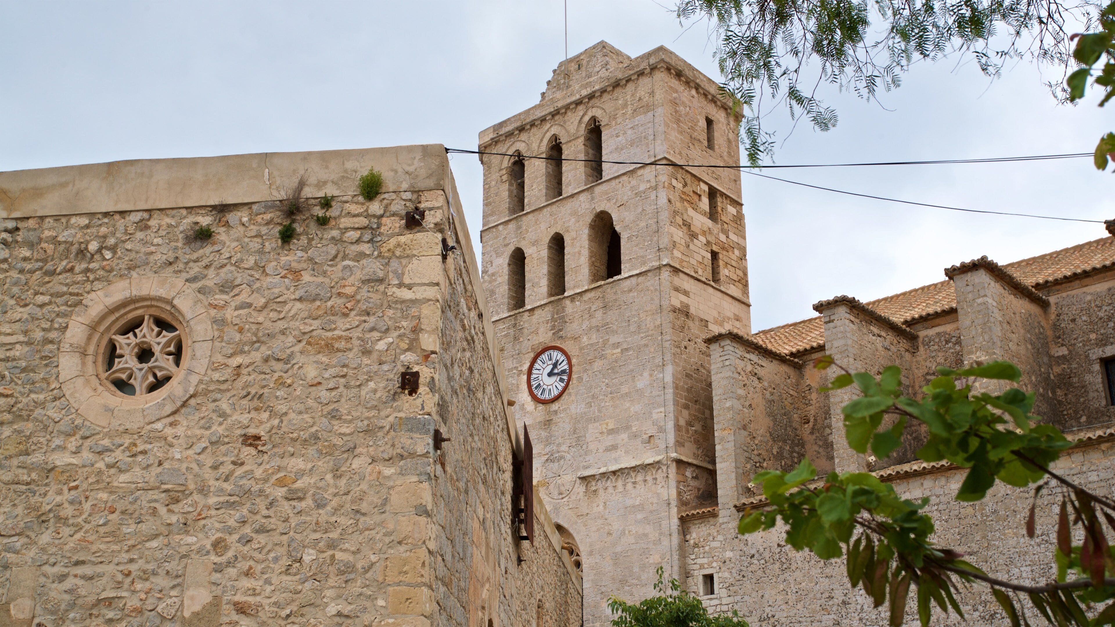 Un edificio histórico de piedra con una torre del reloj y un ventanal redondo con diseño de estrella.