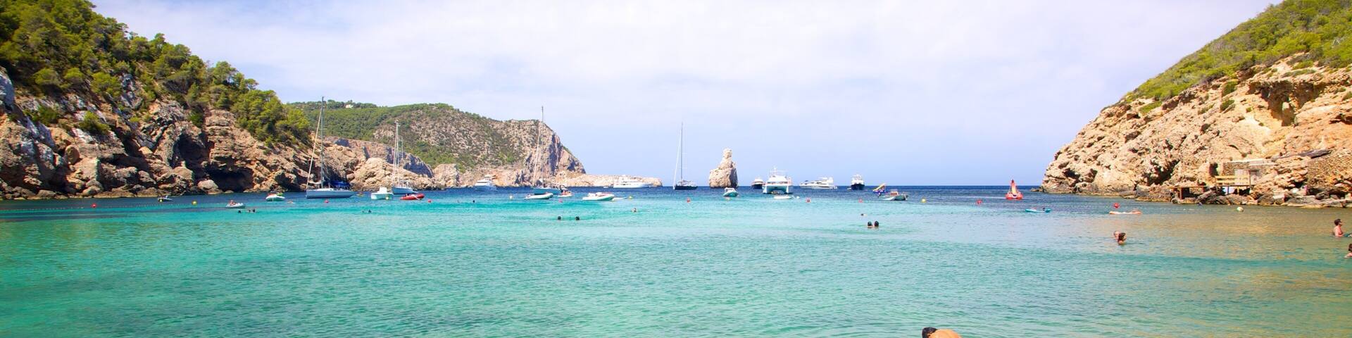 Un mar turquesa transparente con acantilados rocosos, barcos y un faro.
