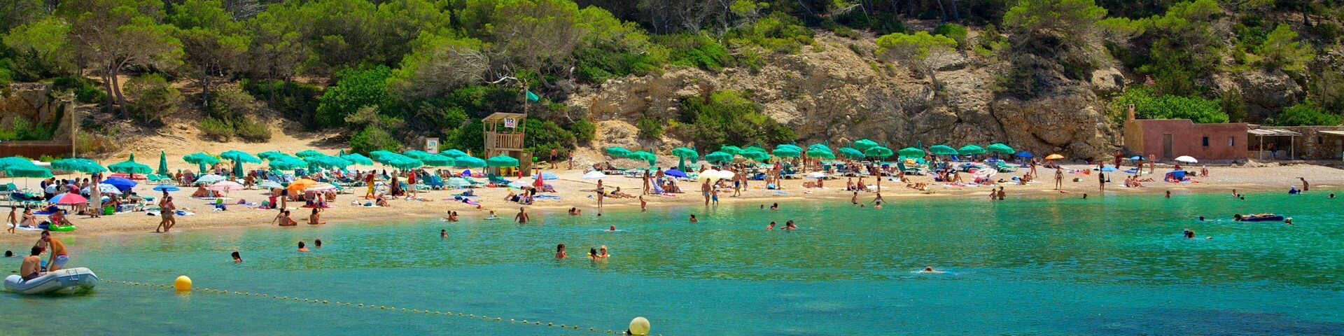 Uma praia com águas turquesa cristalinas, pessoas nadando e tomando sol, e guarda-sóis verdes.