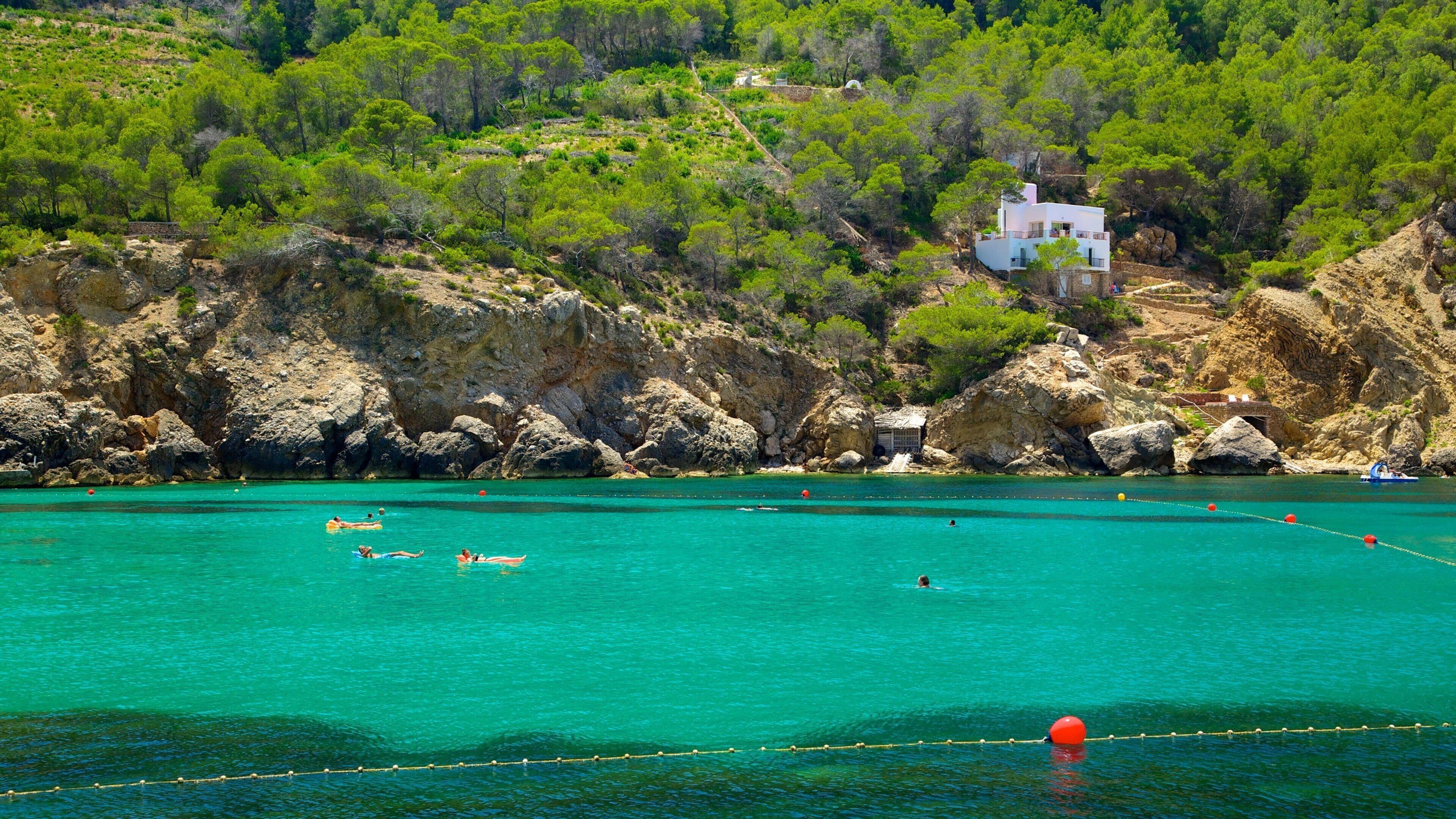 Un paysage côtier caractérisé par une eau turquoise cristalline, des falaises rocheuses et un bâtiment blanc perché sur une colline.