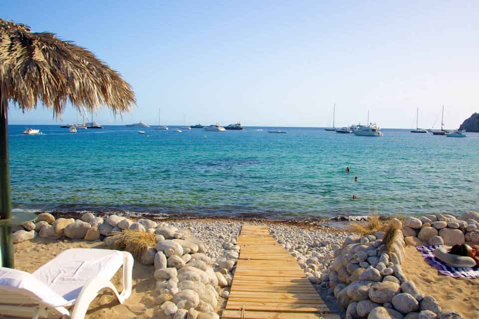 Una playa con un camino de madera, sillas de descanso y una sombrilla de paja.