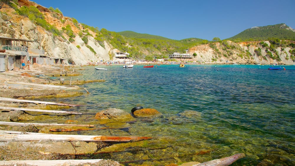 A coastal scene with clear waters, rocky shore, and buildings on the hillside.