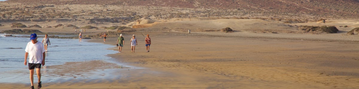 A beach with people walking and a large hill in the background.