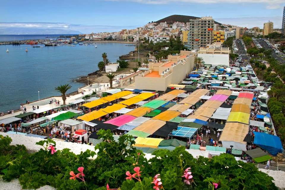 A coastal town with colorful market stalls, a marina, and a hillside with buildings.
