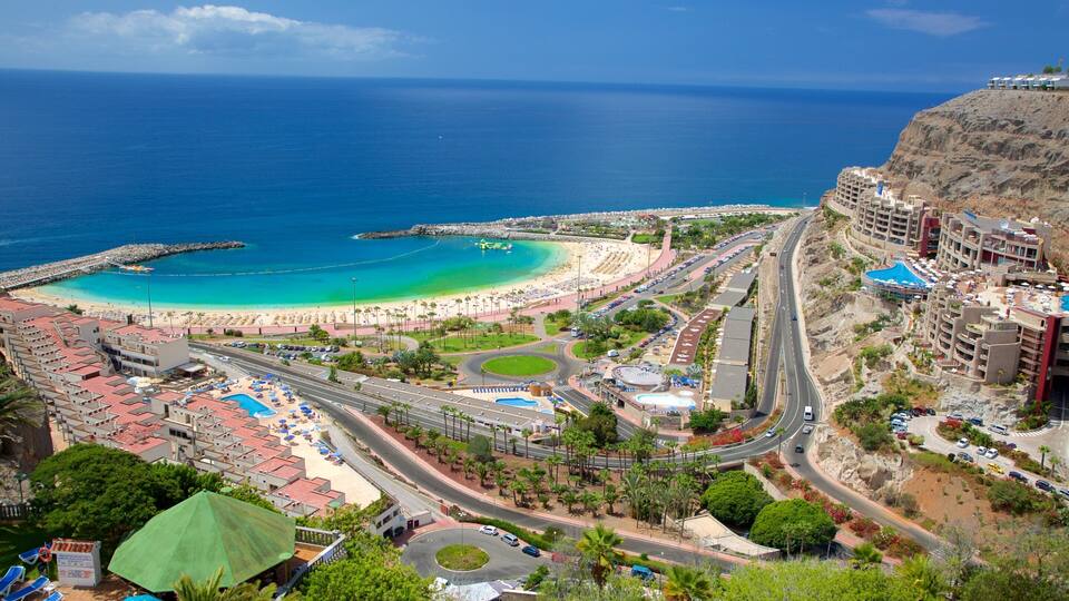 A coastal resort with a beach, a swimming pool, and a mountainous backdrop.