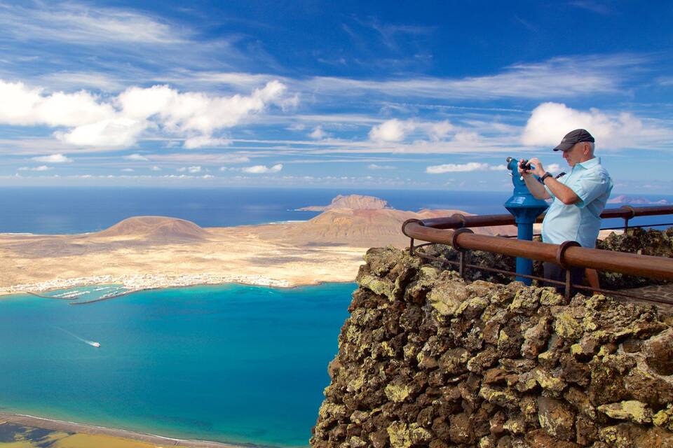 A coastal landscape with a rocky cliff, turquoise waters, and a small town.