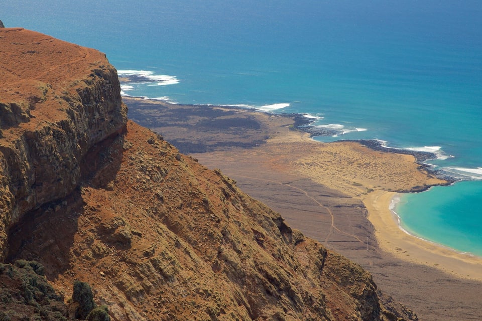 Un paysage côtier avec une falaise rocheuse, une plage de sable et des vagues turquoise.