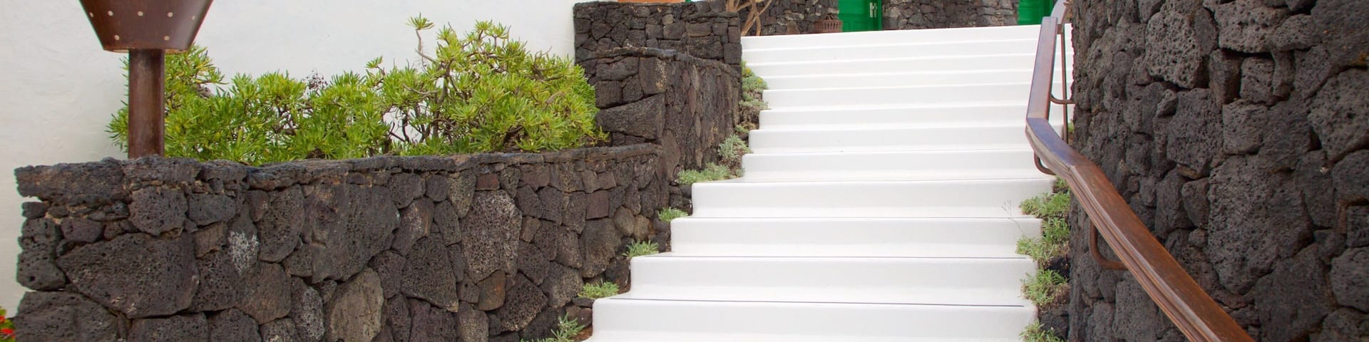 A white staircase with green doors, a stone wall, and a metal lamp post.