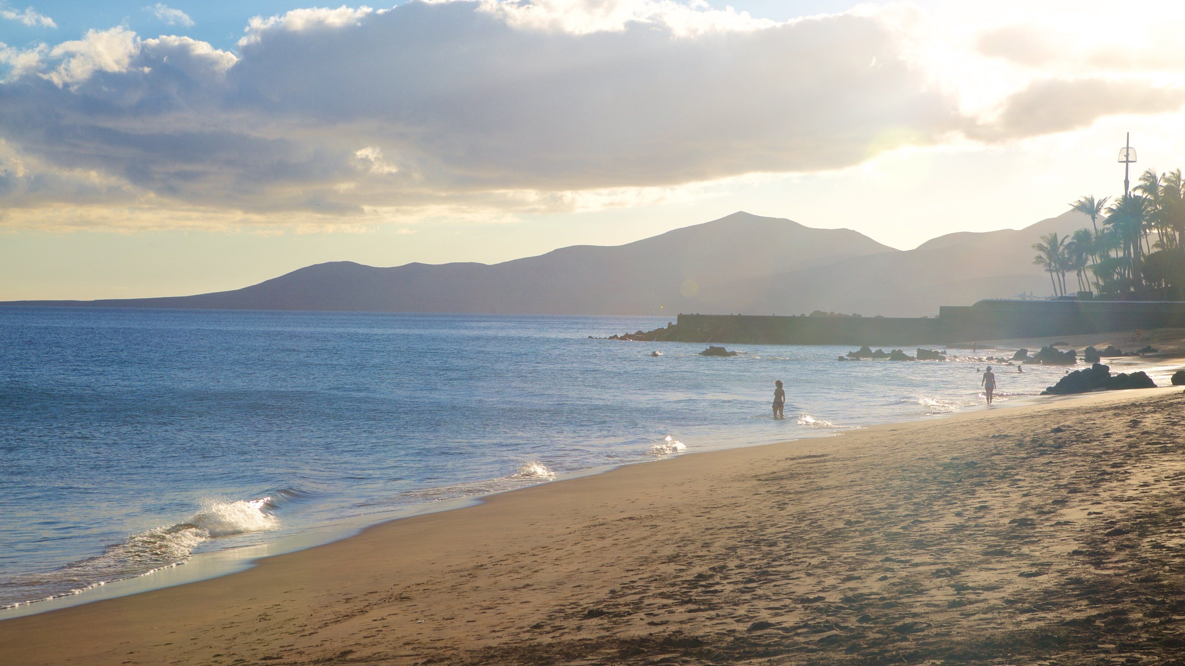 A beach with calm waters, a sandy shore, and distant mountains.