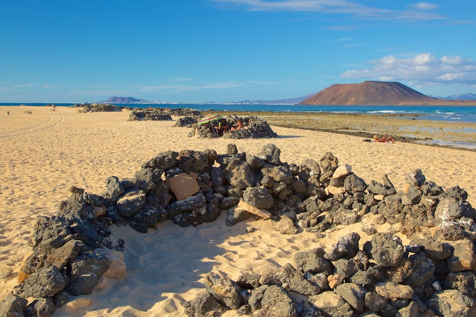 Eine felsige Formation an einem sandigen Strand mit einem Berg im Hintergrund.