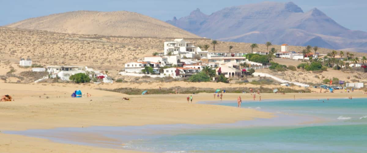 A beach with people, a mountain, and buildings.