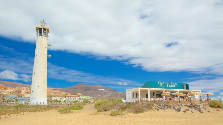 Un faro, el bar Beach Bar El Faro, y un paisaje desértico con montañas al fondo.